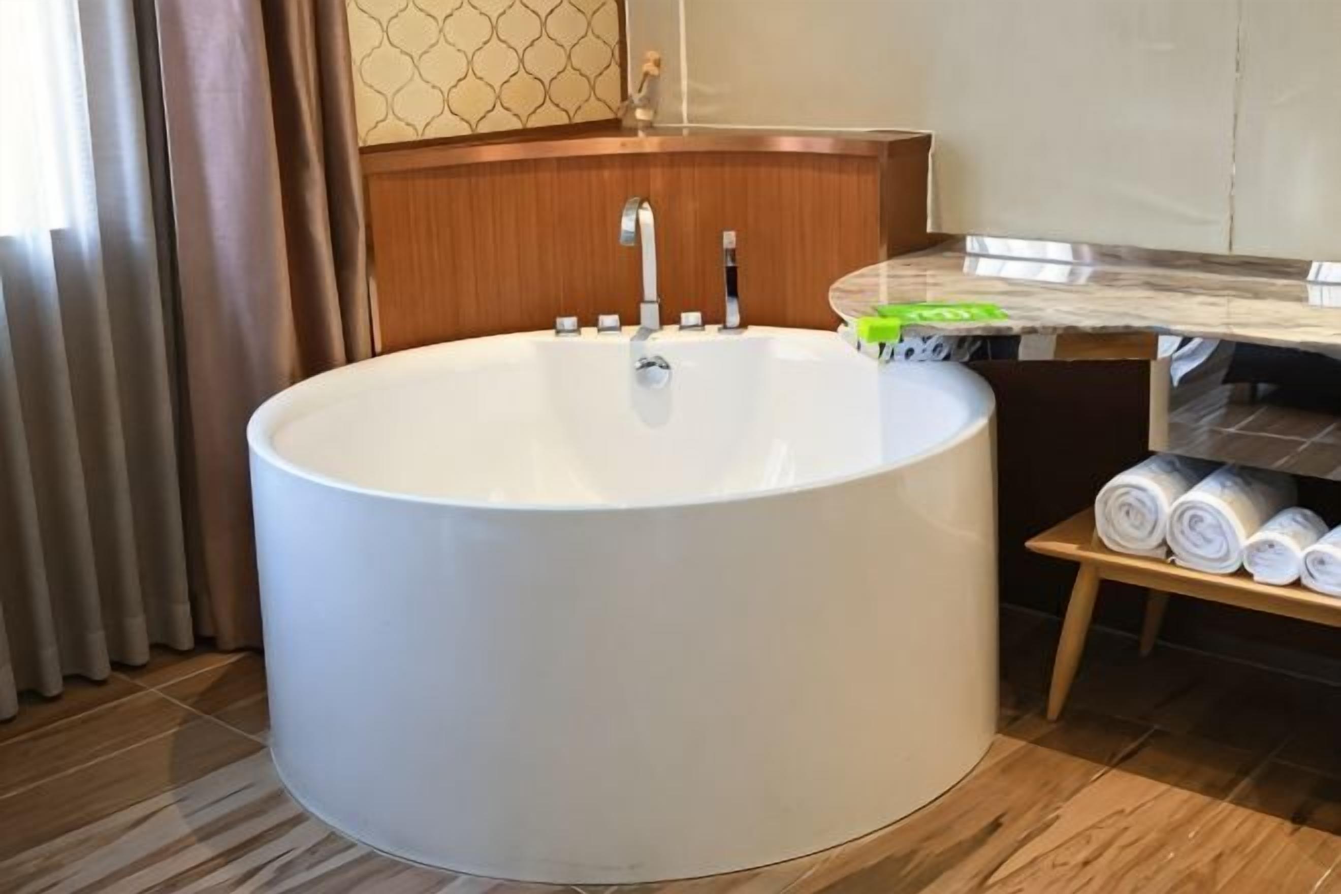 Una bañera grande y redonda en un baño con un tocador de madera y un perchero para toallas.