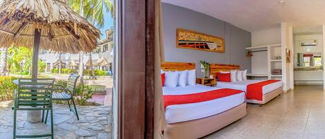 A hotel room with two beds, a wooden headboard, and a view of the outdoor area with a thatched umbrella and palm trees.