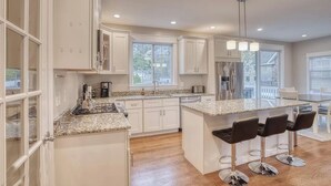 A modern kitchen with white cabinetry, granite countertops, a stainless steel refrigerator, and a bar area with stools. - Waterfront Escape! NYC Ferry, Beach, Modern New Construction 3 bedroom 3 bath (Highlands)