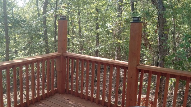 A wooden deck with railings overlooking a forested area. - HICKORY HIDEOUT
The cabin is surrounded by a large area of trees for privacy (Mena)