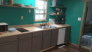A kitchen with a microwave, sink, and dishwasher. There are shelves above the counter holding dishes and cups. - HICKORY HIDEOUT
The cabin is surrounded by a large area of trees for privacy (Mena)