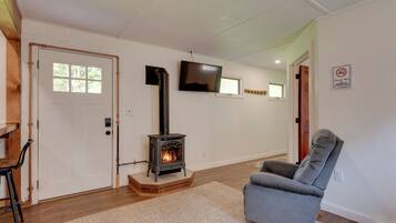 A living room with a wood-burning stove, a grey armchair, and a television mounted on the wall.