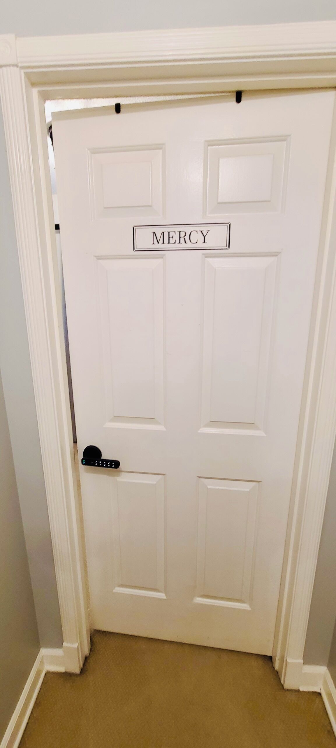 A white door with a nameplate reading "MERCY" and a modern electronic lock.