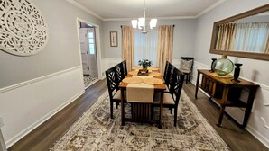 A dining room with a wooden table, black chairs, a patterned rug, a chandelier, and a mirror on the wall. - Memphis Retreat w/ Sunroom, Pool Table, Retro Gaming, Gym & Relaxing Vibe (Memphis)