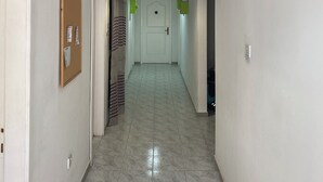 A hallway with a teal pendant light, a bulletin board, and a door leading to a room.