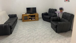 A living room with a sofa, two armchairs, a coffee table, and a TV on a wooden stand.