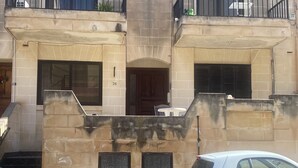 A building with a stone facade, numbered 36, featuring a small balcony with a table and chairs, and a car parked in front.