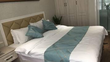 Una cama bien hecha con una colcha blanca y azul, un cabecero color beige y una mesita de noche con una lámpara.