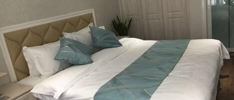 Una cama bien hecha con una colcha blanca y azul, un cabecero color beige y una mesita de noche con una lámpara.