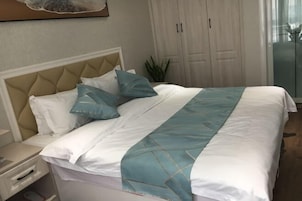 Una cama bien hecha con una colcha blanca y azul, un cabecero color beige y una mesita de noche con una lámpara.