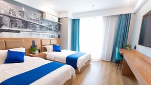 Et hotelværelse med to senge, et skrivebord, en stol og et bybillede på væggen.
