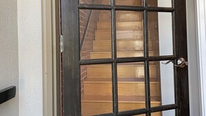 Une porte en bois sombre, ornée d’un motif en croisillons, qui donne sur un escalier avec des marches en bois et un mur en briques.