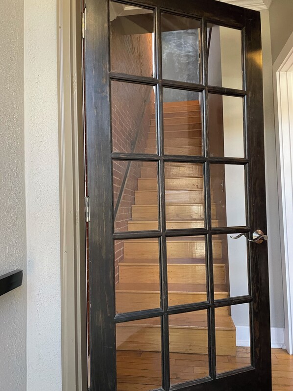 Una puerta de madera oscura con un diseño de cuadrícula, que da a una escalera de peldaños de madera y un muro de ladrillo.