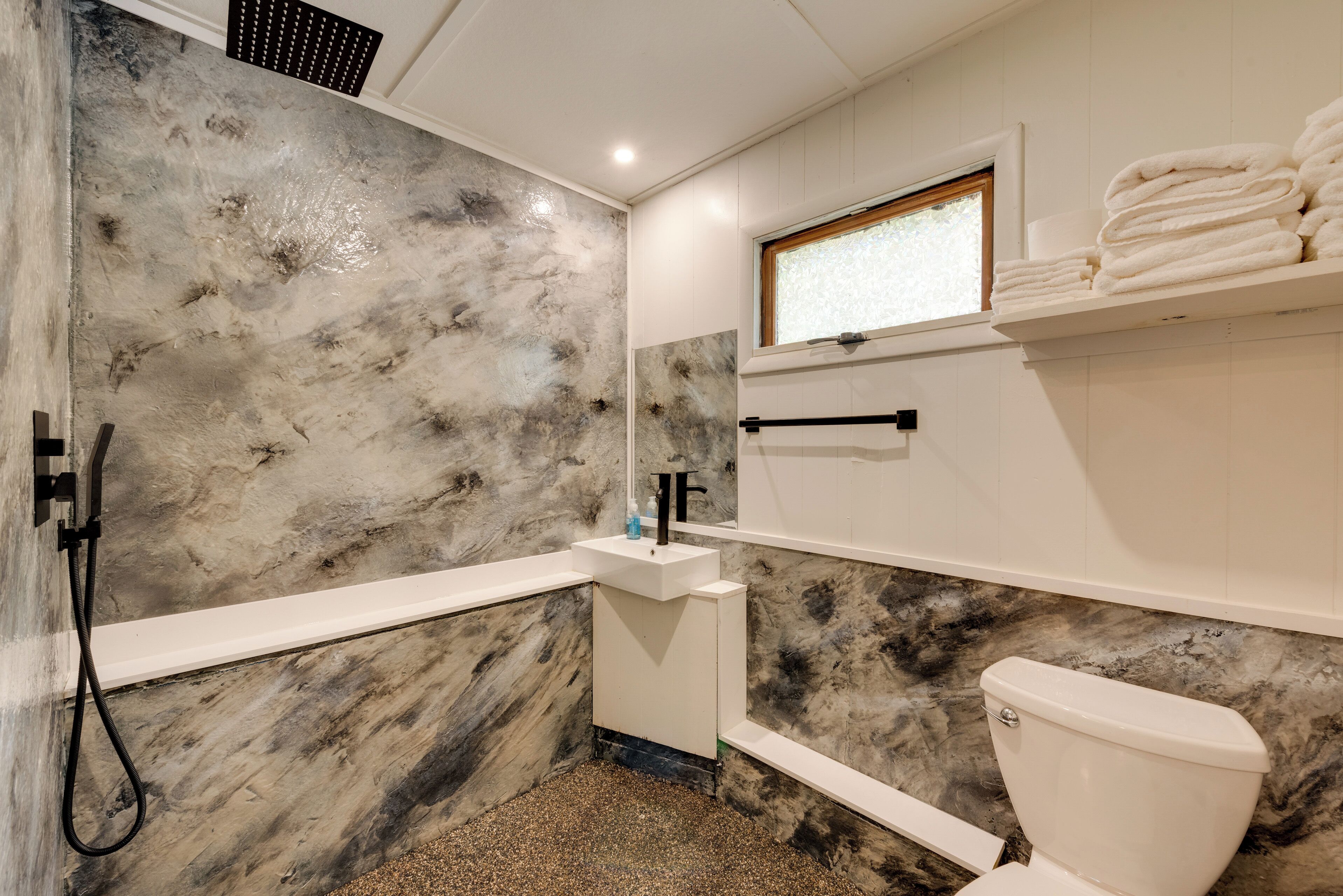 A bathroom with a marble wall, a white sink, a toilet, and a towel rack.