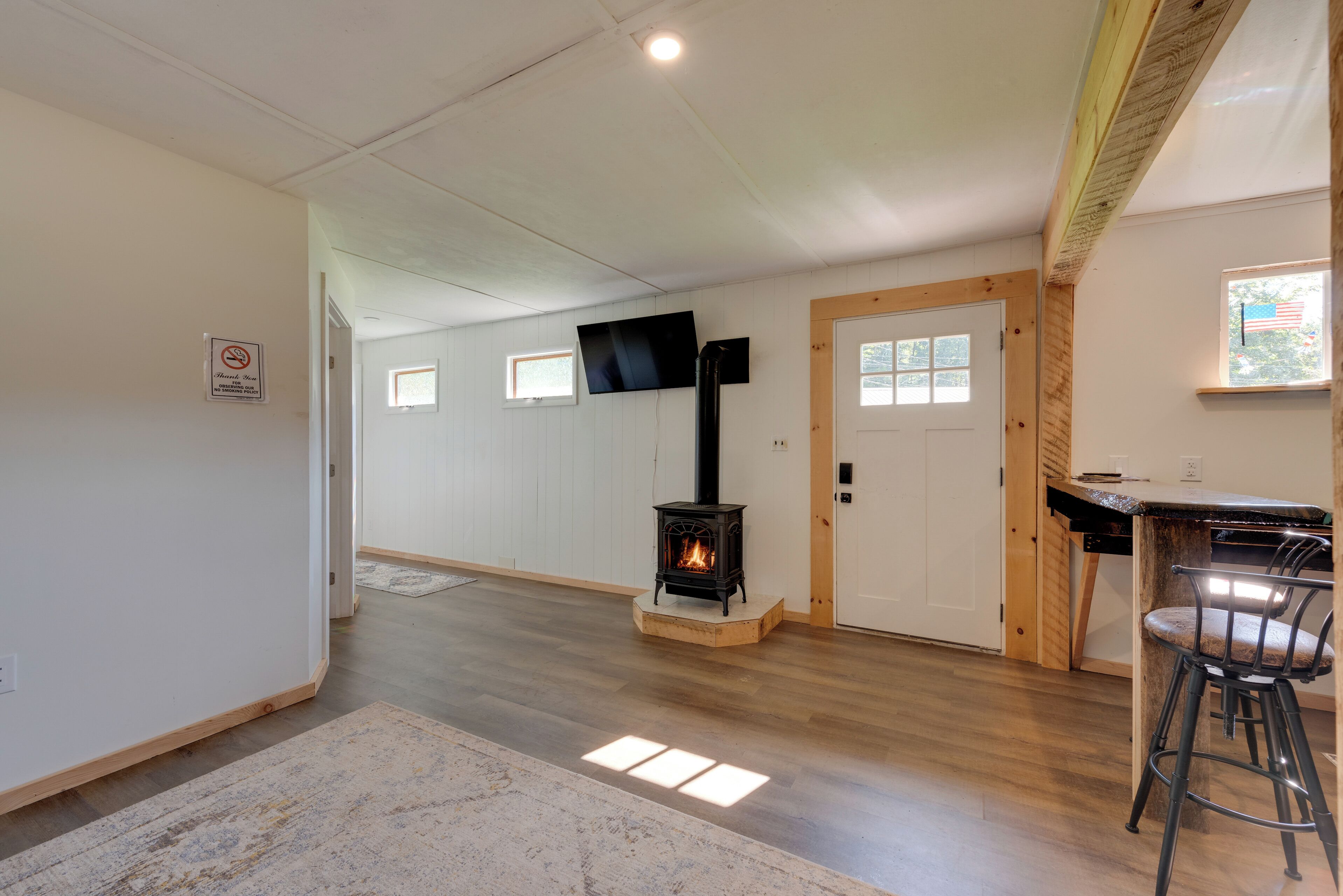 A spacious room with a wood-burning stove, a television mounted on the wall, and a small window with an American flag.
