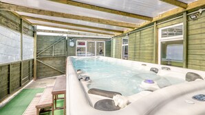 Un jacuzzi con muelle de madera y una pequeña mesa, rodeado por una valla de madera y un área cubierta con puerta de vidrio.