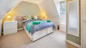 Un dormitorio con techo inclinado, una cama con cubrecama gris y azul, dos lámparas de noche y una ventana con vistas al exterior.