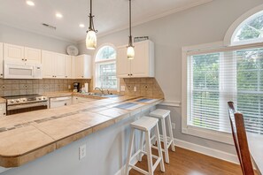 A kitchen with white cabinets, a built-in microwave, a stove, and a large island with bar stools.