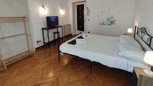 Una camera d'albergo con un letto, una scrivania con un computer, una sedia, un termosifone e una porta.