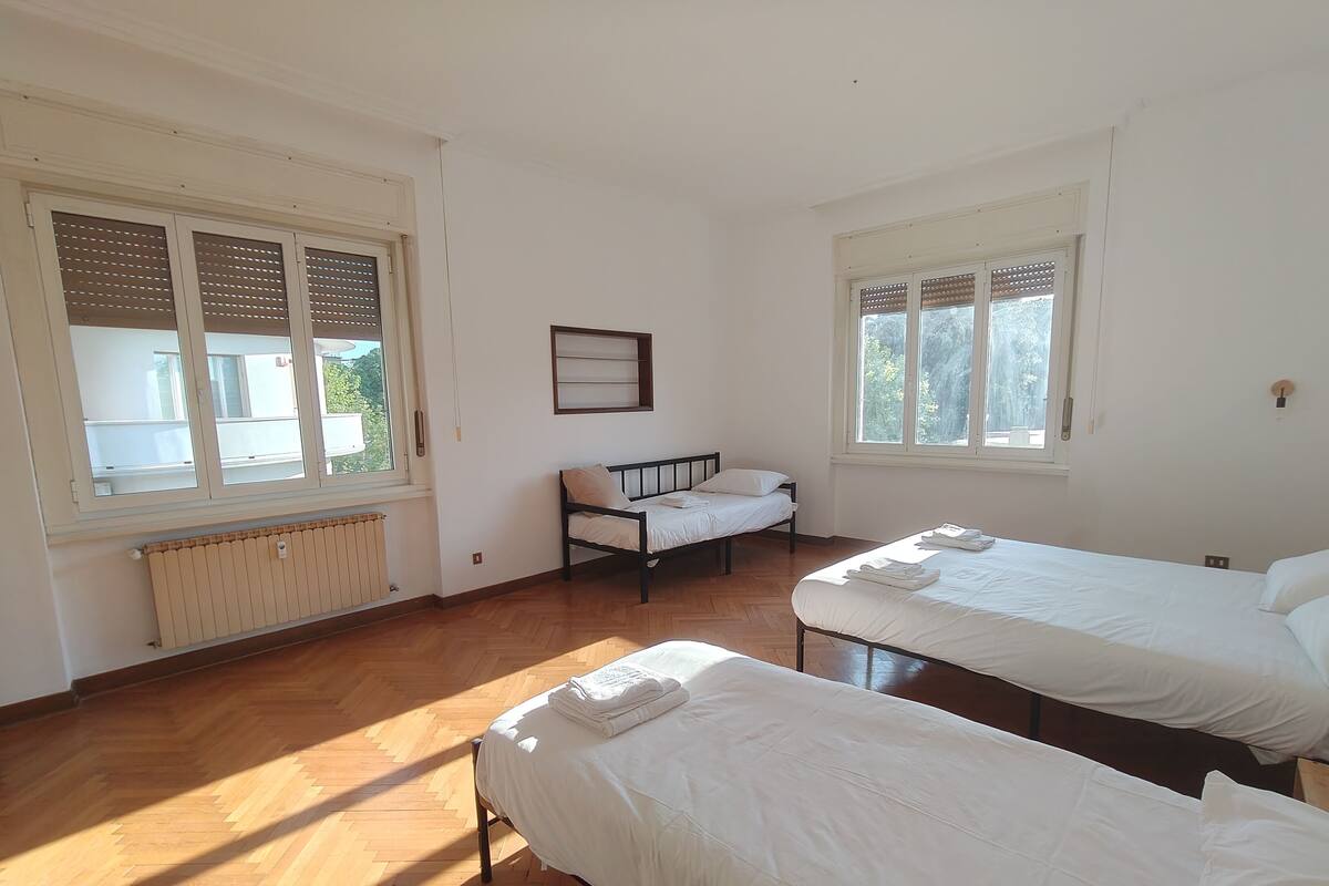 A room with two beds, a radiator, and large windows with blinds.