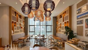 Un comedor de hotel con mesas redondas, lámparas colgantes de mimbre y un mostrador de buffet.