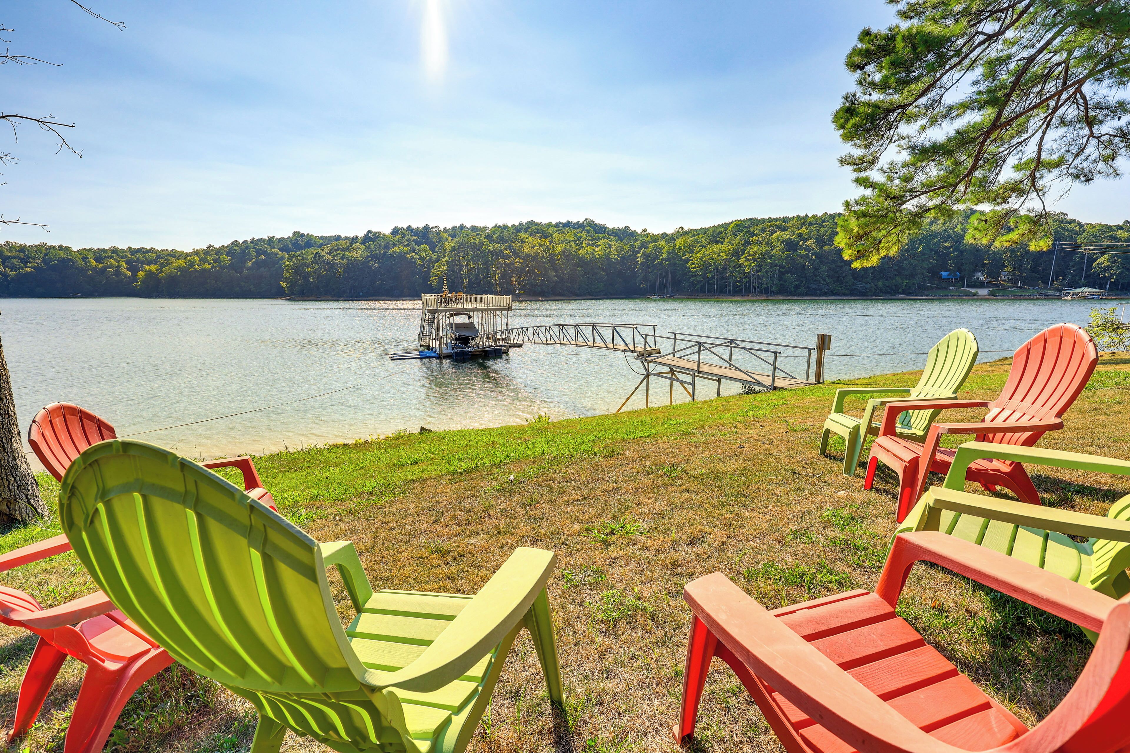 A lakeside view with a dock, chairs, and a boat.