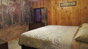 A bedroom with a bed, wooden walls, a ceiling fan, and a forest mural. - Cozy 2-bedroom cabin in front of the lake!!! (Mannford)