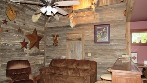 A rustic interior with a brown leather sofa, a wooden bar, and various wall decorations including stars and animal heads. - Cozy 2-bedroom cabin in front of the lake!!! (Mannford)