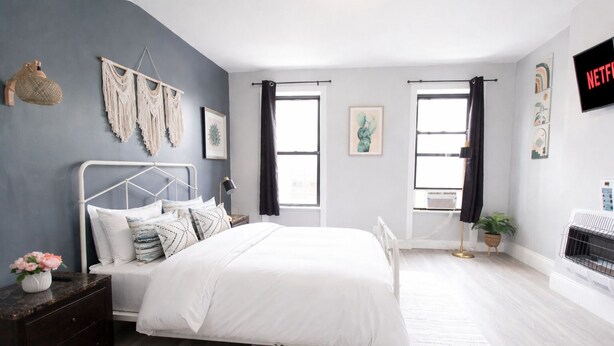 A modern bedroom with a bed, bedside tables, a wall-mounted macrame piece, and a fireplace. - 𖡡 First Street Flat - 1BR Apt just 15 Min to NYC (Hoboken)