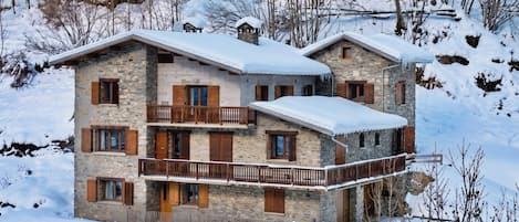Un edificio de varios pisos de piedra con un balcón, rodeado de árboles cubiertos de nieve.