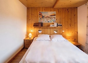 Et soveværelse med træpaneler, seng, sengeborde, lampe og et billede hængende på væggen.