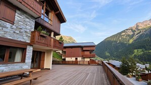 Una terraza de madera con un muro de piedra, balcones de madera y vistas a la montaña.