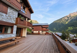 A wooden deck with a stone wall, wooden balconies, and a mountain view.