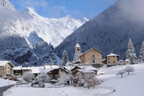 Un village de montagne enneigé, avec des bâtiments traditionnels, une église et une vue dégagée sur les montagnes environnantes.