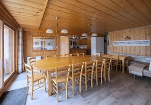 Et træinteriør med et stort spisebord, stole og hængende lamper.