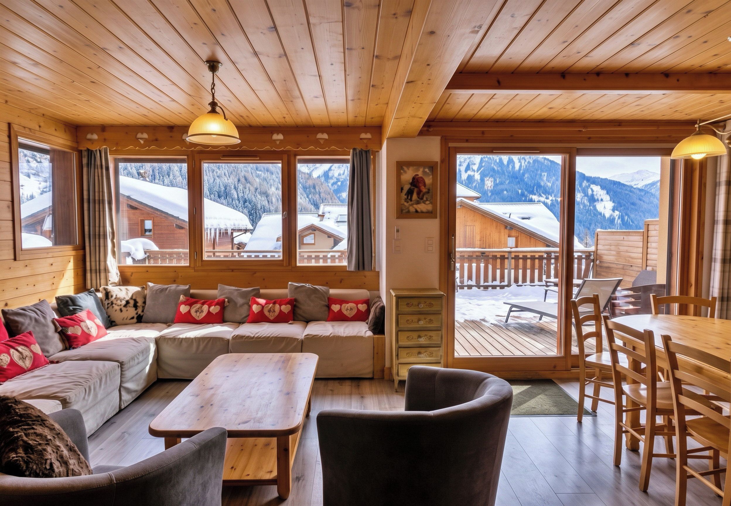 Een gezellig houten interieur met een bank, stoelen, een tafel en een uitzicht op besneeuwde bergen door grote ramen.