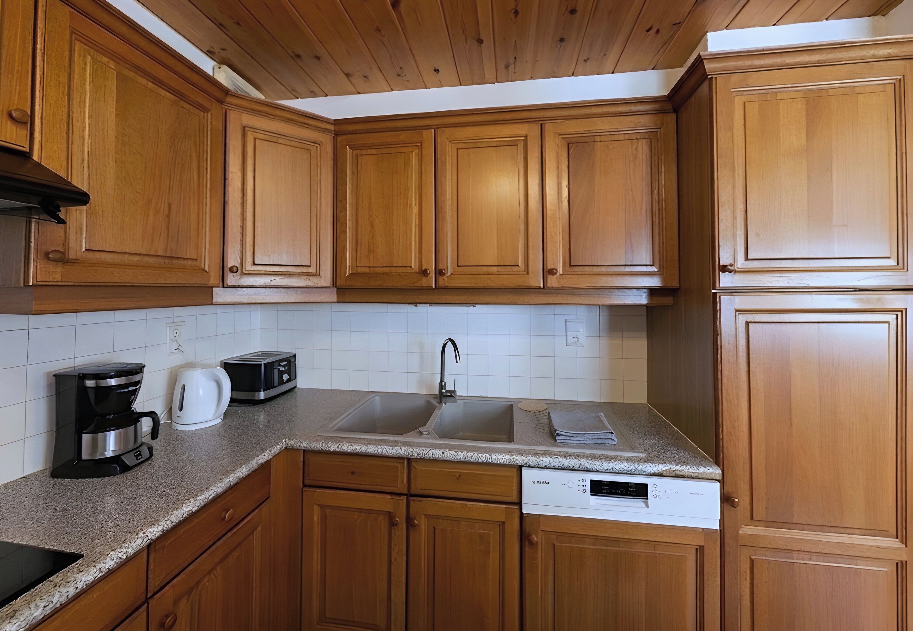 A kitchen with wooden cabinets, a stainless steel sink, a coffee maker, a toaster, and a dishwasher.