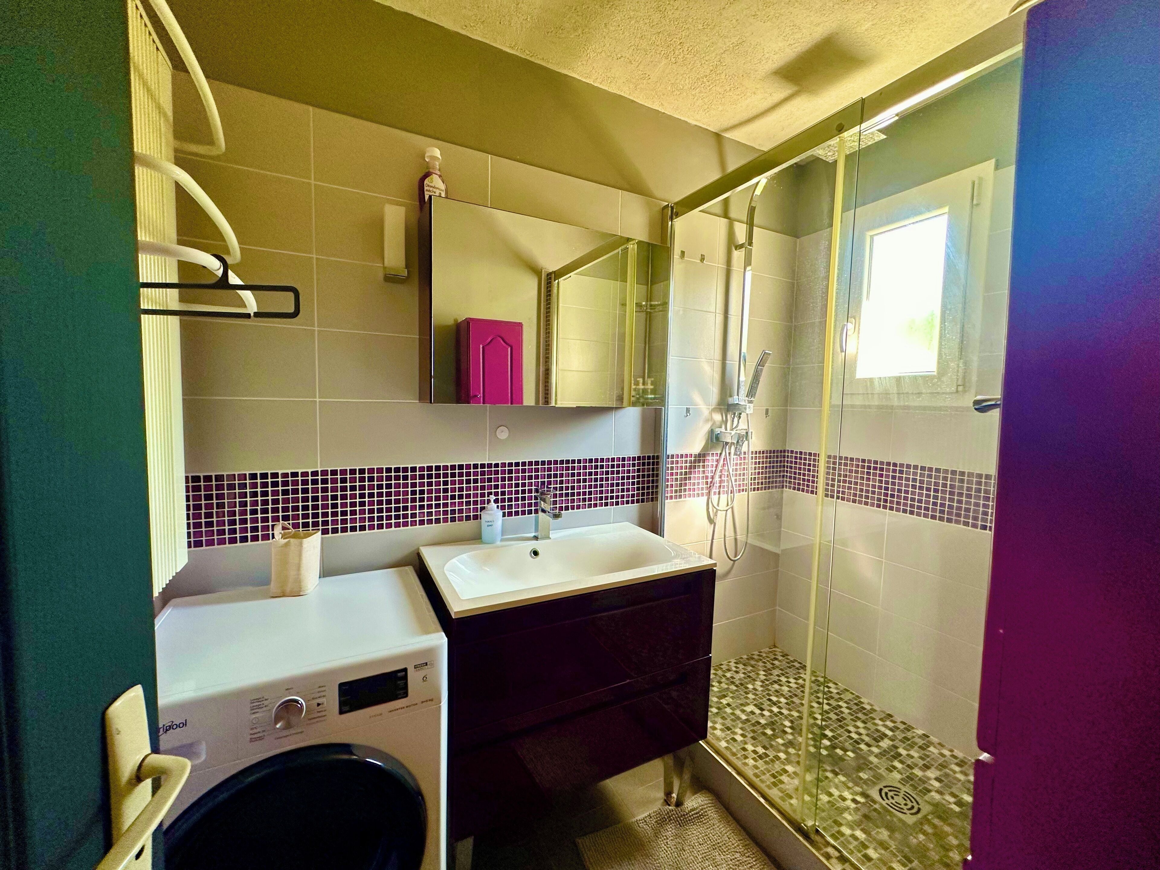 Un baño con lavadora, lavabo, espejo y zona de ducha.