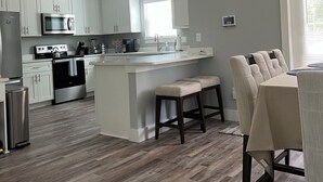 Una cocina moderna con gabinetes blancos, un microondas de acero inoxidable y una isla grande con taburetes.