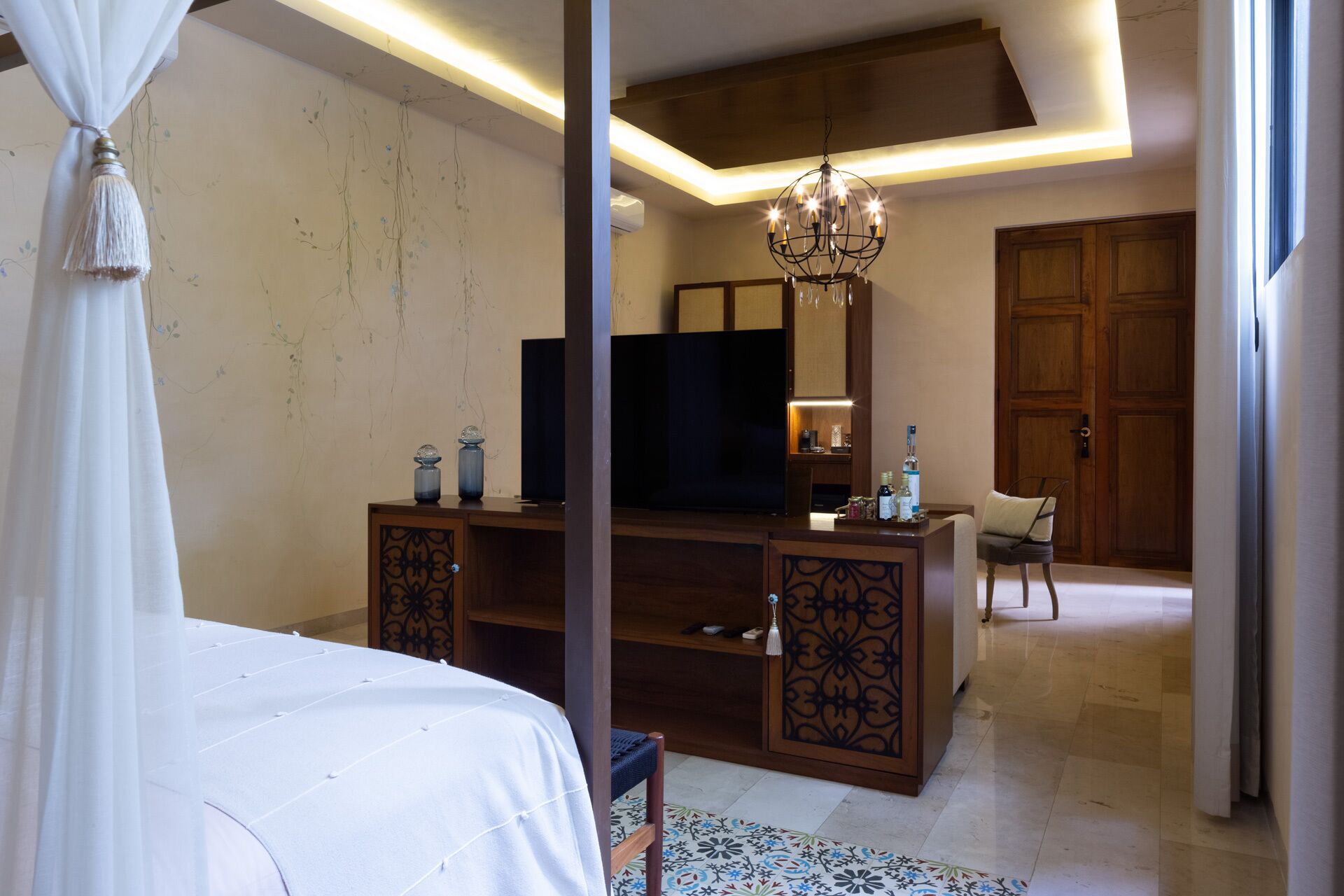 Un dormitorio con cama, escritorio, televisor, candelabro y puerta.