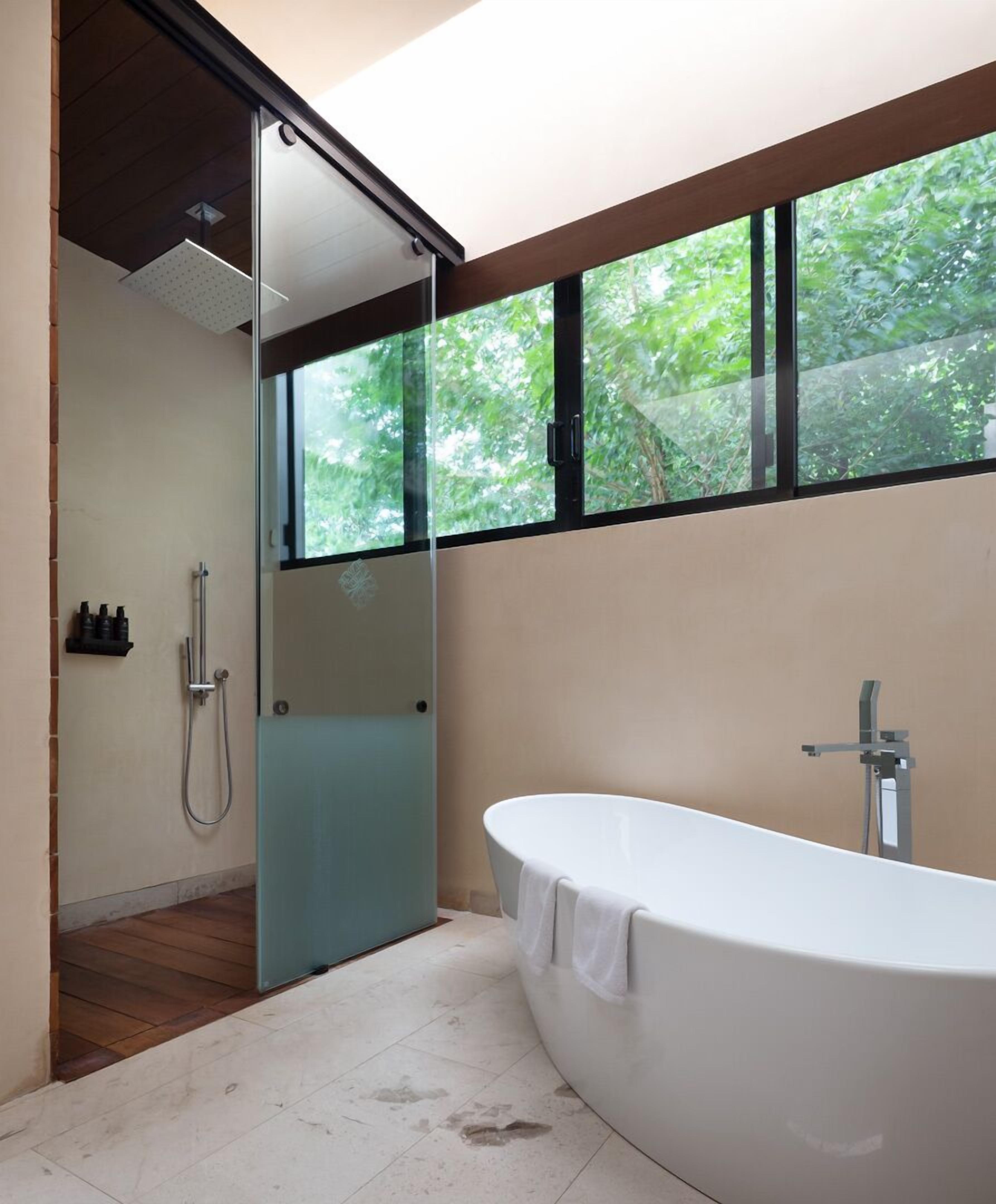 A modern bathroom with a freestanding bathtub, a glass shower enclosure, and a large window offering a view of greenery.