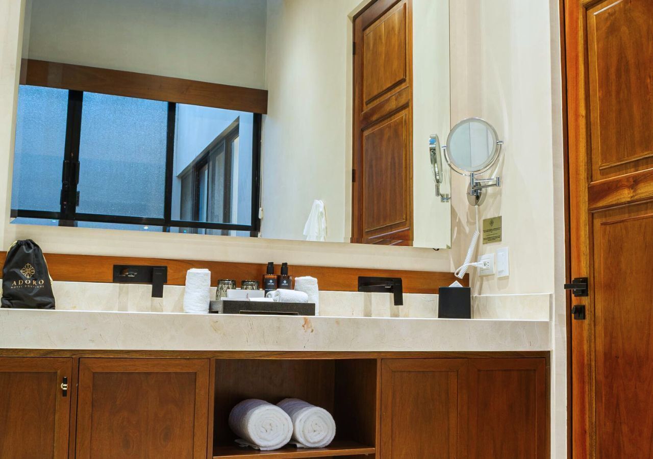 Une salle de bain avec un meuble-lavabo en bois, un miroir, un distributeur de serviettes et une étagère où sont pliées des serviettes.