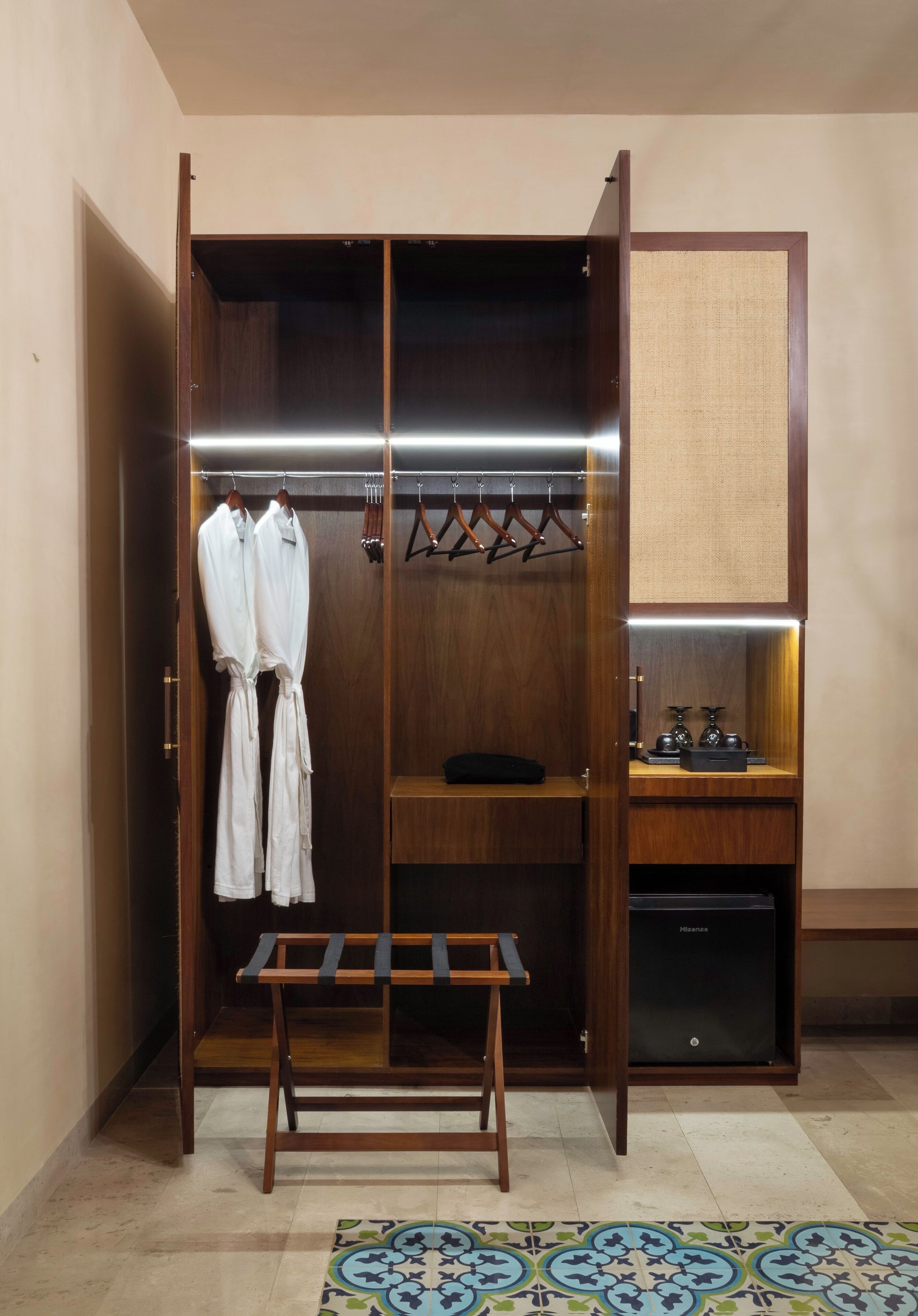 A walk-in closet with a bench, hanging clothes, and a small shelf with items.