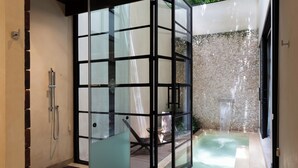 A glass-enclosed spa area with a hot tub, a shower, and a stone wall. - Adoro Hotel Boutique (Mérida)