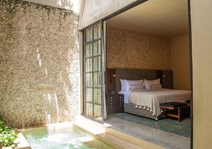 A bedroom with a bed, a bench, a nightstand, and a water feature.