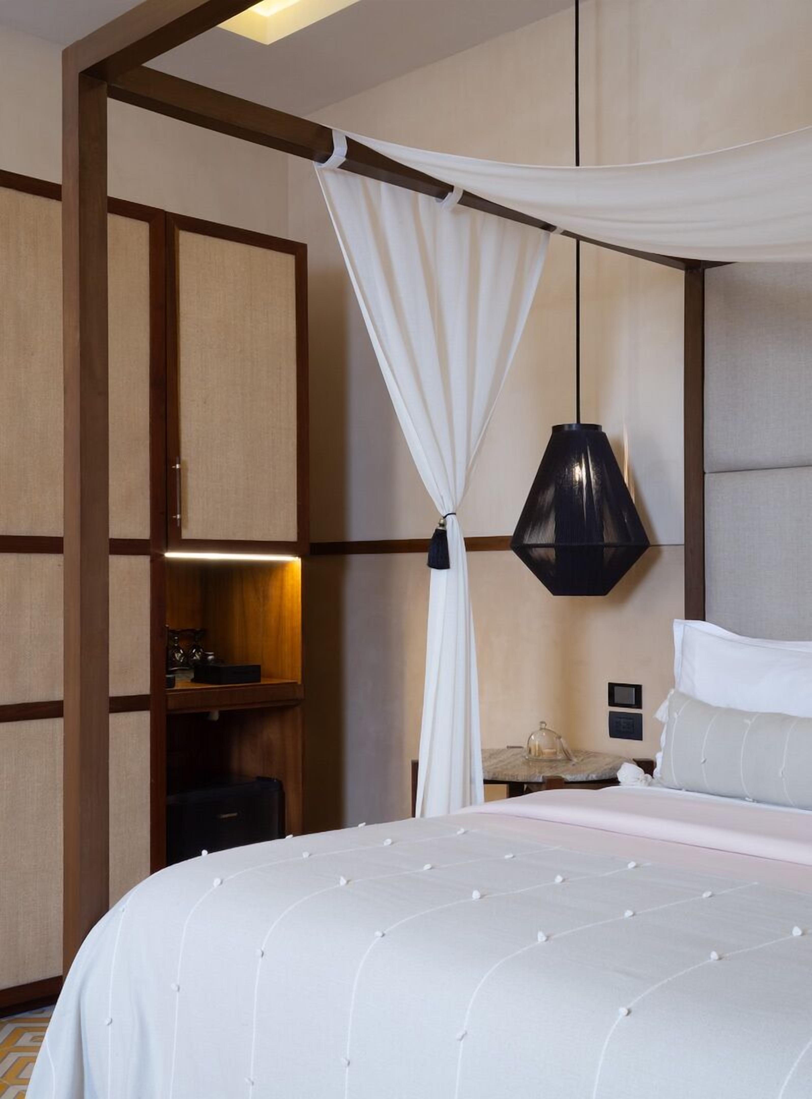 A hotel room with a canopy bed, a bedside table, a lamp, and a wardrobe.