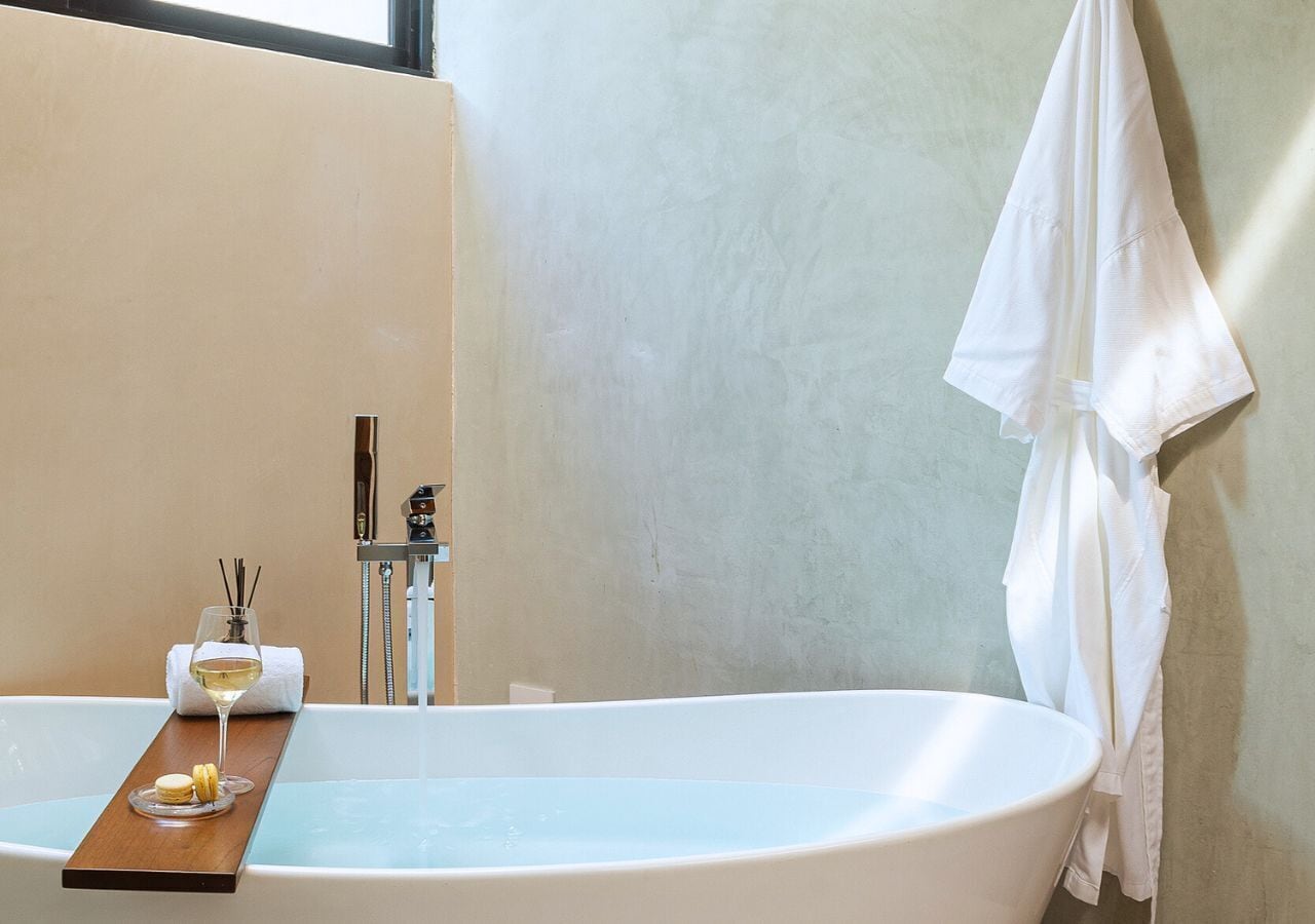 A modern bathroom with a freestanding bathtub, a glass of wine, and a tray with snacks.