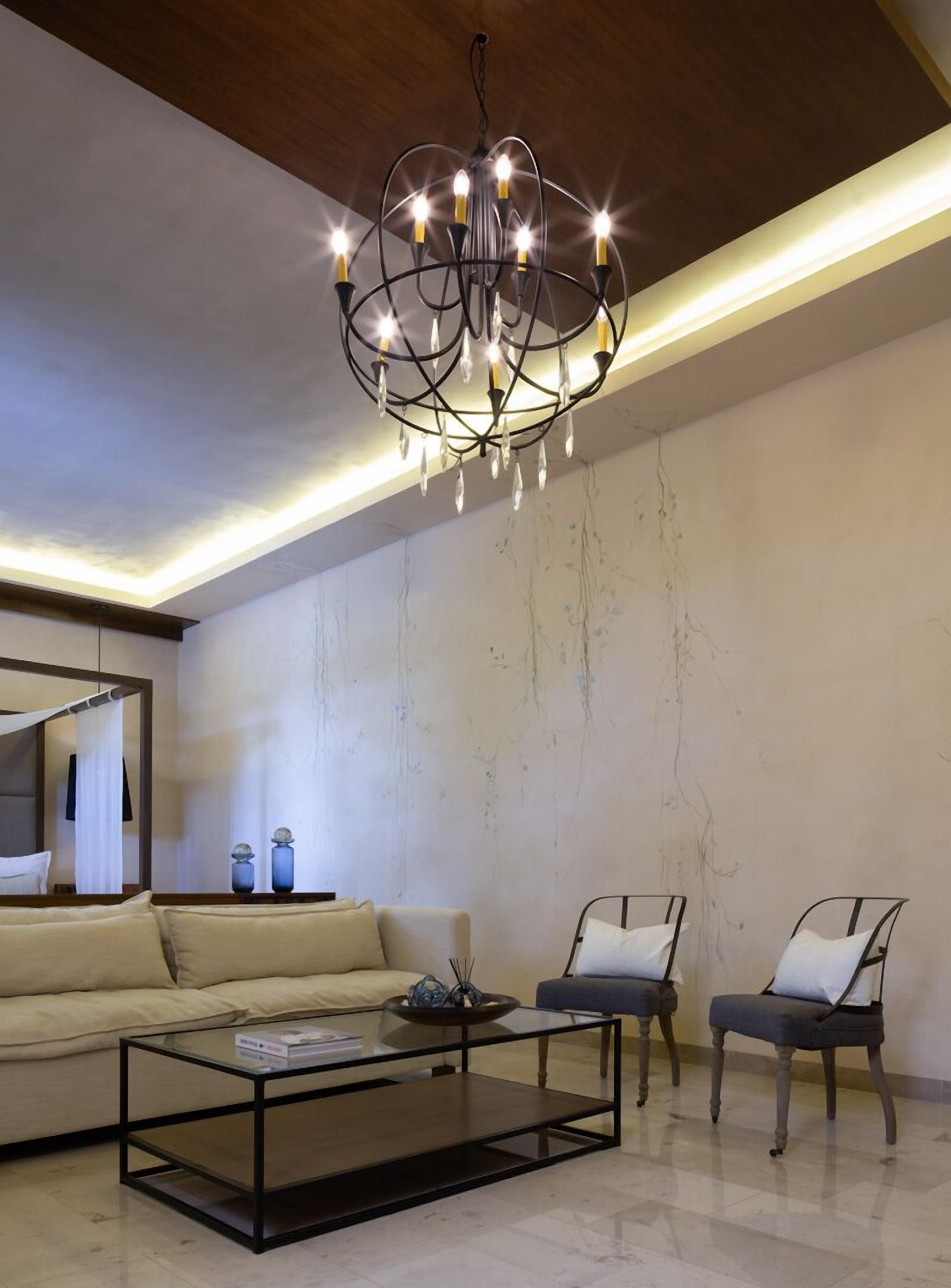 Uma sala de estar moderna com uma mesa de centro de vidro, um sofá, duas poltronas, um candelabro e teto de madeira.