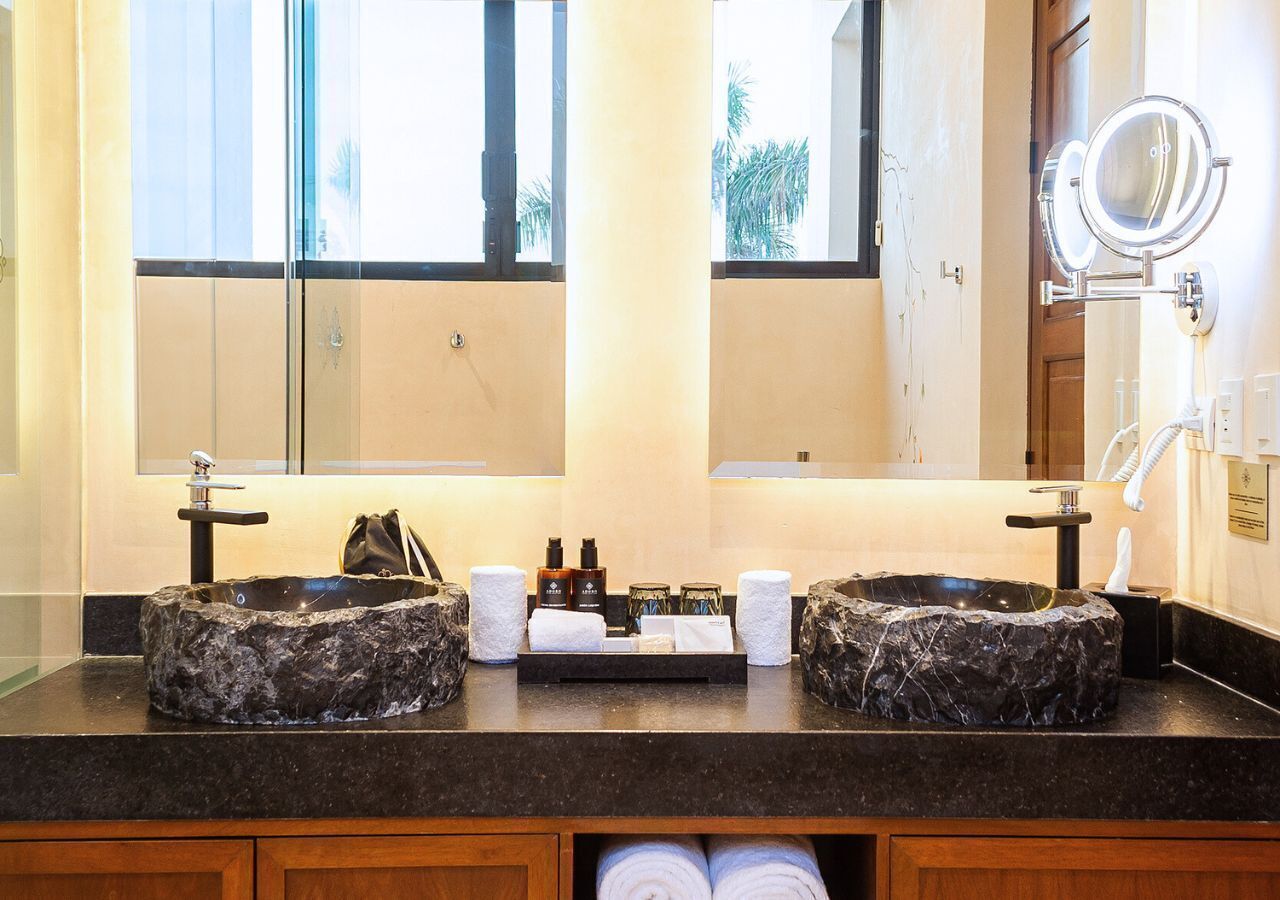Un baño con dos lavamanos de mármol, un espejo grande y un perchero para toallas.