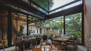 An indoor dining area with wooden tables and chairs, surrounded by greenery and stone walls. - Adoro Hotel Boutique (Mérida)